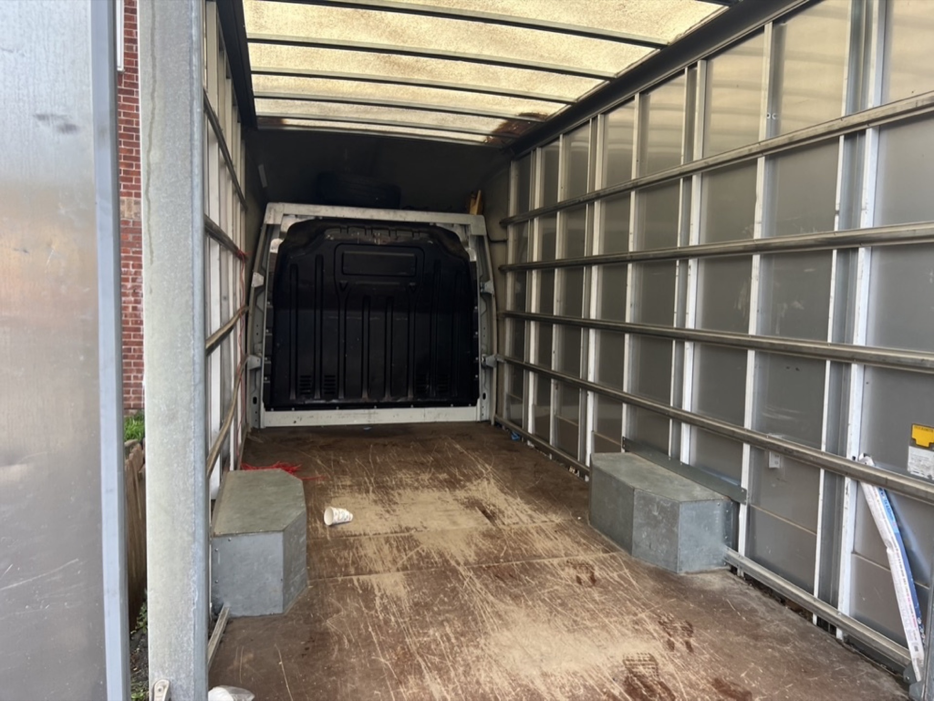 Empty Luton box van interior with bare aluminium walls and a dirty plywood floor
