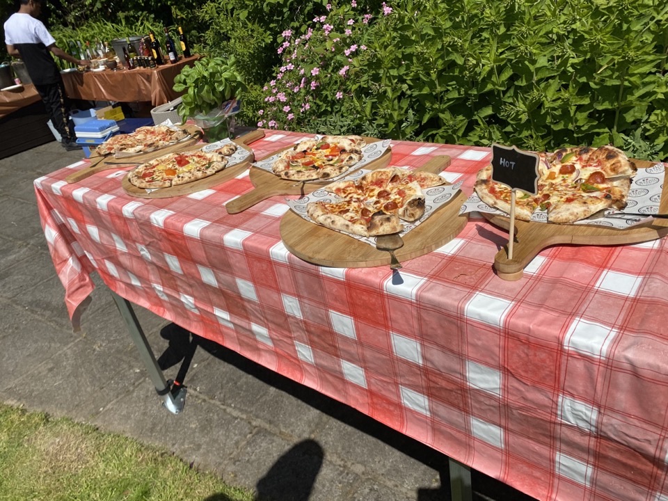 Whole pizzas on branded boards along a red gingham table, each labelled for guests