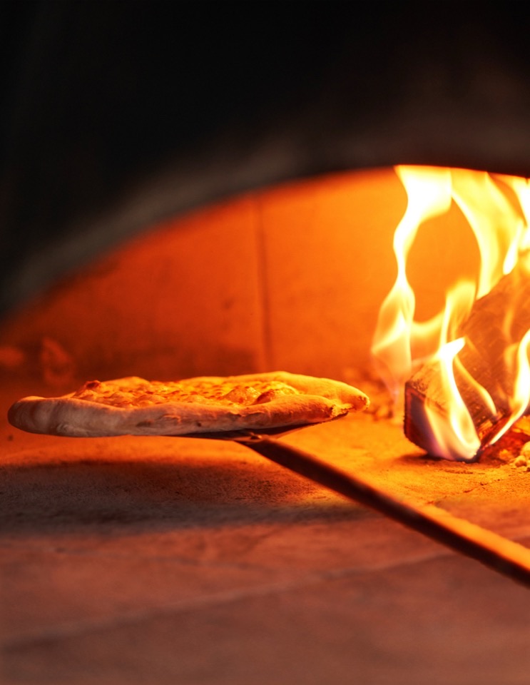 A pizza on a peel inside a glowing oven