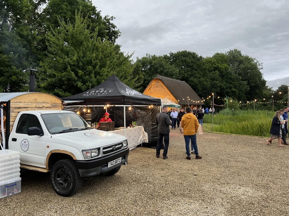 The pizza truck and branded gazebo serving guests at an evening barn event