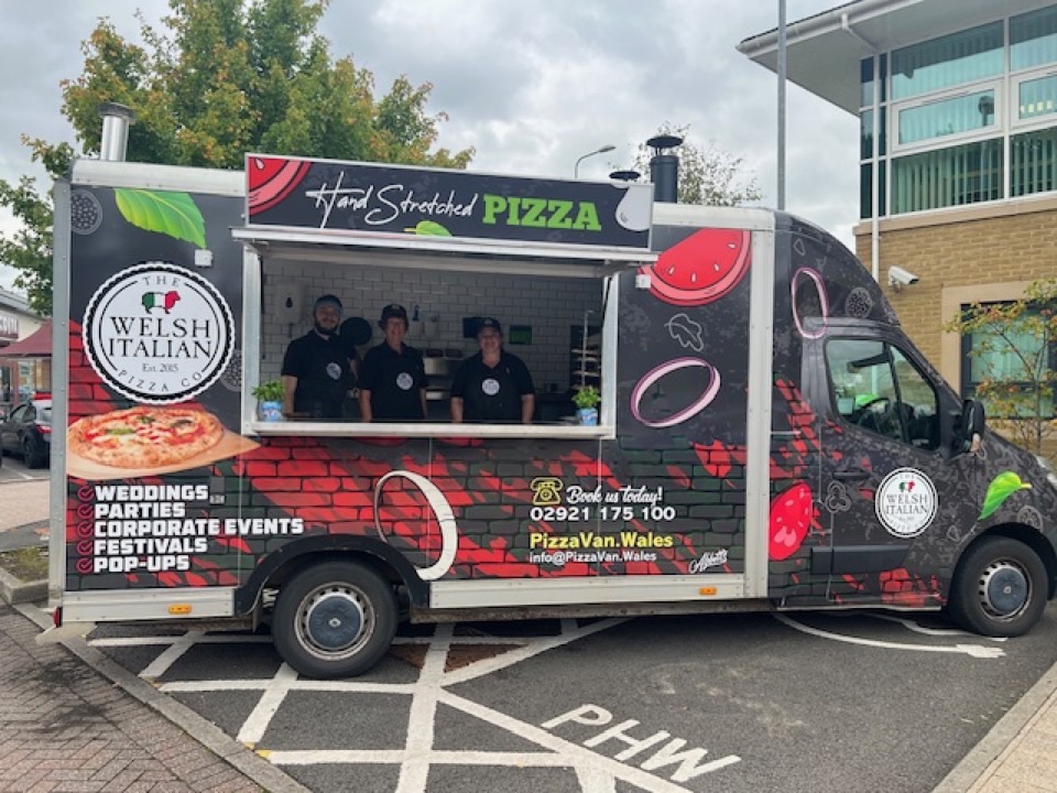 The Welsh Italian Pizza Co black wrapped pizza van with the crew serving from the hatch
