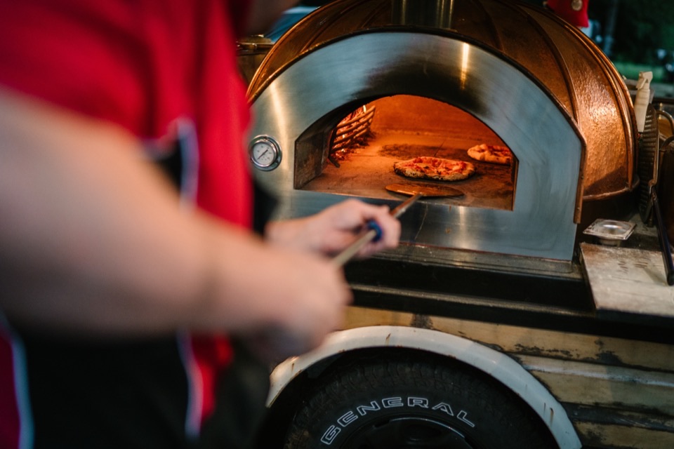 A pizza going into the copper-domed oven on the peel at a wedding